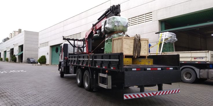 Camião com grua carregado com equipamento, junto a um armazém