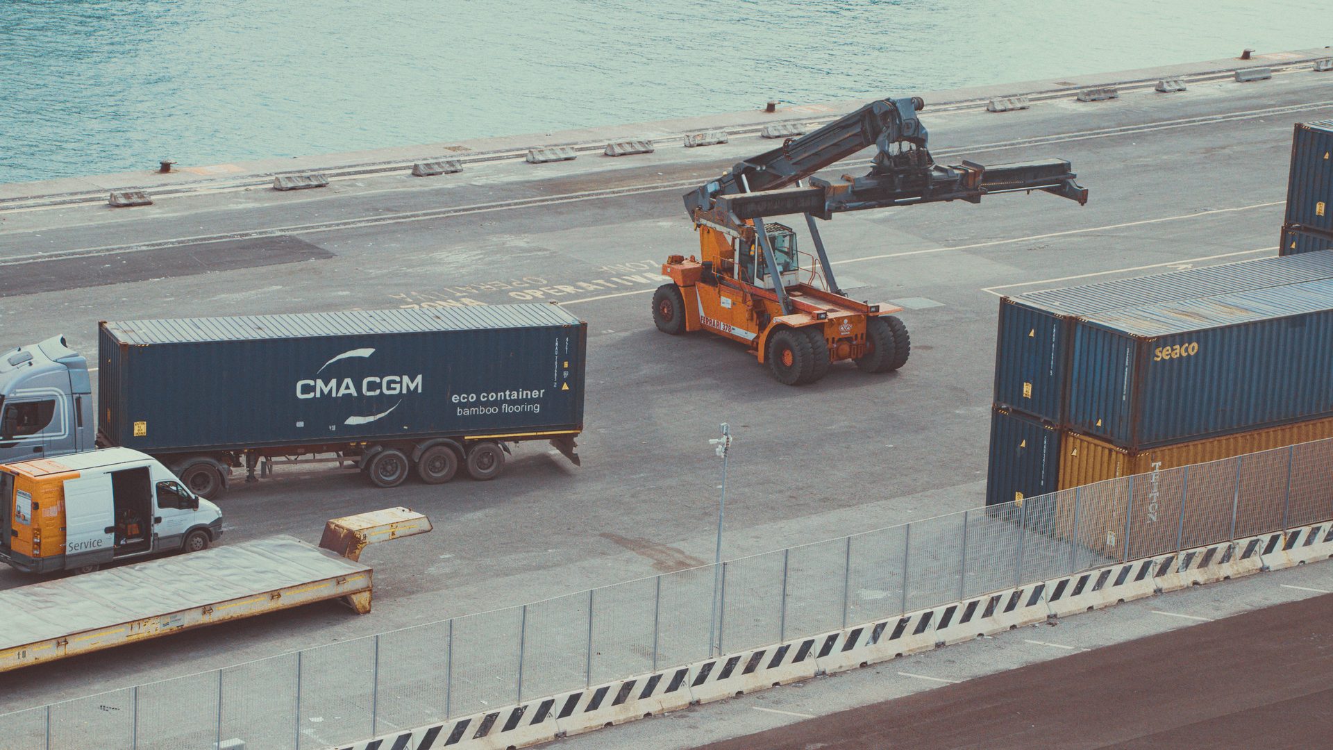 Empilhador de contentores a manobrar no cais, junto a um contentor da CMA CGM