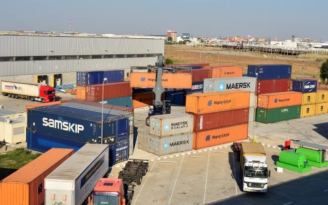 Parque de contentores com empilhadores e camiões em movimento